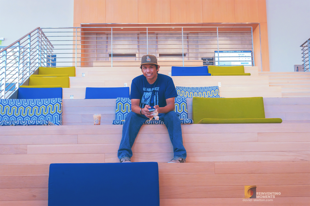 About Me 7 Gio is sitting on Social Stairs in CSUSB Student Union, intently checking his phone, with empty stairs around, symbolizing the calm before the spring semester rush.
