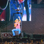 Kenny Chesney held aloft by fans at a packed Rose Bowl stadium, bathed in stage lights.