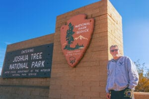 Maximizing Your One-Day Adventure in Joshua Tree National Park 1 It's me, David Skelton, standing next to the Joshua Tree National Park sign at the North Entrance, with a picturesque desert and Joshua trees in the background.