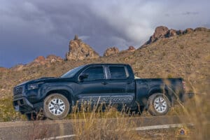 Vegas Jets and River Runs 3 Black 2022 Nissan Frontier SV parked on Arizona highway with Thumb Butte in the background.