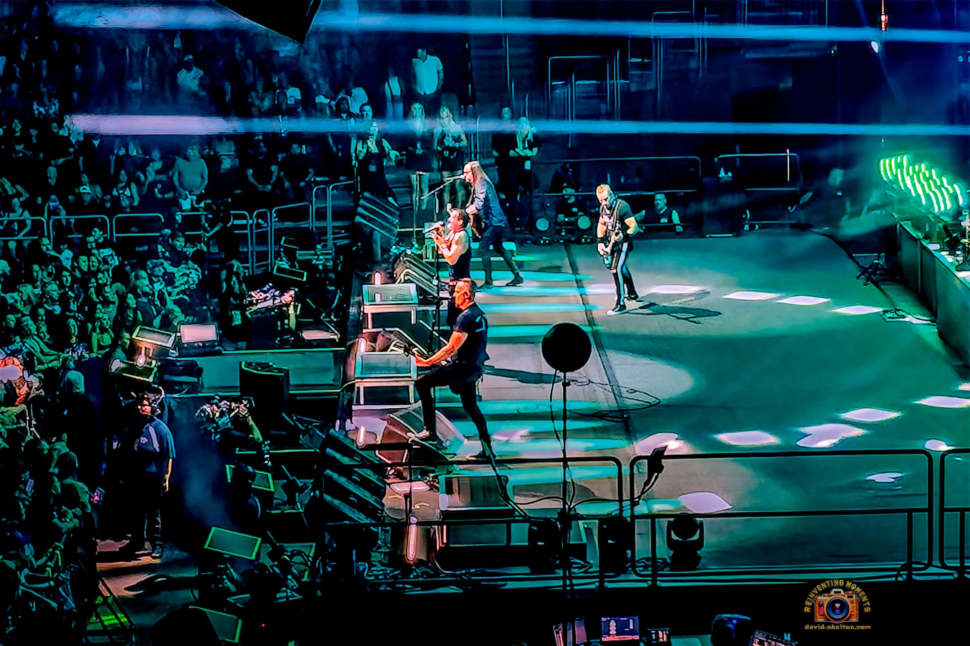 Wide shot of the rock band Creed performing on a large, blue-lit stage in a packed arena, with singer Scott Stapp on the left and a massive speaker array hanging from the ceiling.