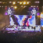 From the crowd, a wide shot of country artist Jordan Davis performing on a brightly lit stage with large video screens and dramatic lighting at the Acrisure Arena.