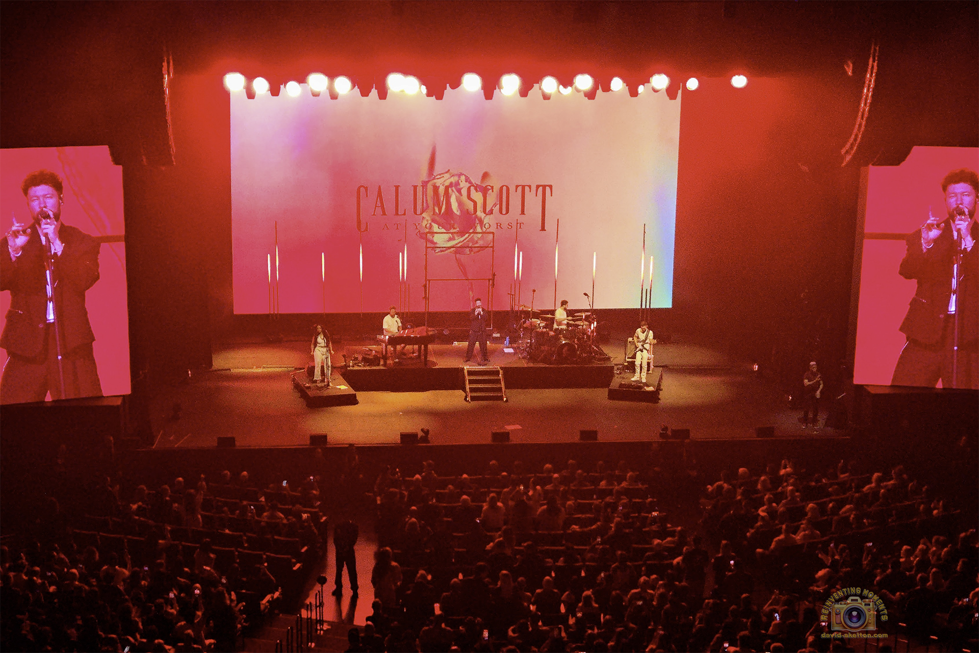 Calum Scott singing "No Matter What" on stage at the Yaamava Resort & Casino, with his drummer and keyboard player on either side of him.