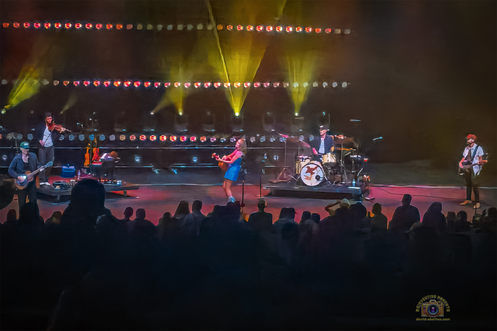 Carly Pearce singing and playing guitar on stage at the Pacific Amphitheatre during her 2025 Hummingbird Tour at the OC Fair. The stage is lit with colorful lights, and the audience is visible in silhouette.