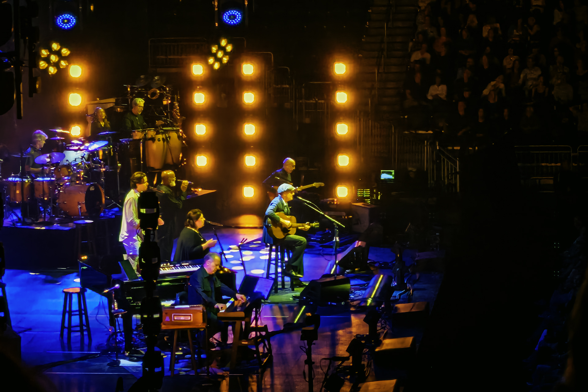 James Taylor and band performing live on stage with blue and orange lighting