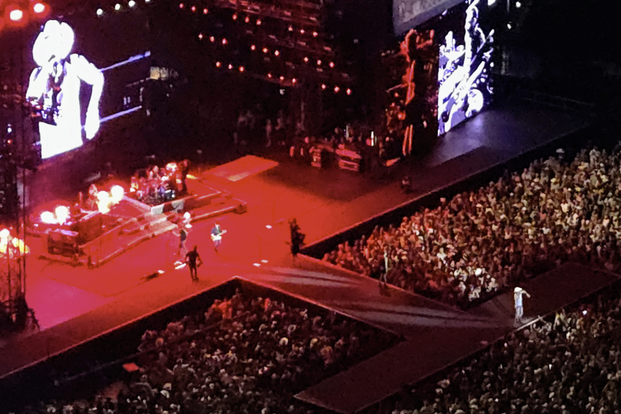 Kenny Chesney singing "Summertime" close-up on the extended stage at SoFi Stadium with large video screens behind him displaying live footage