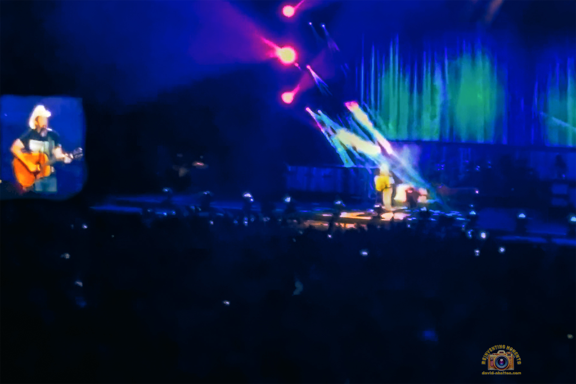 A wide stage view of Brad Paisley performing on the Weekend Warrior Tour, with a large video screen showing him playing guitar and the stage lit in blue