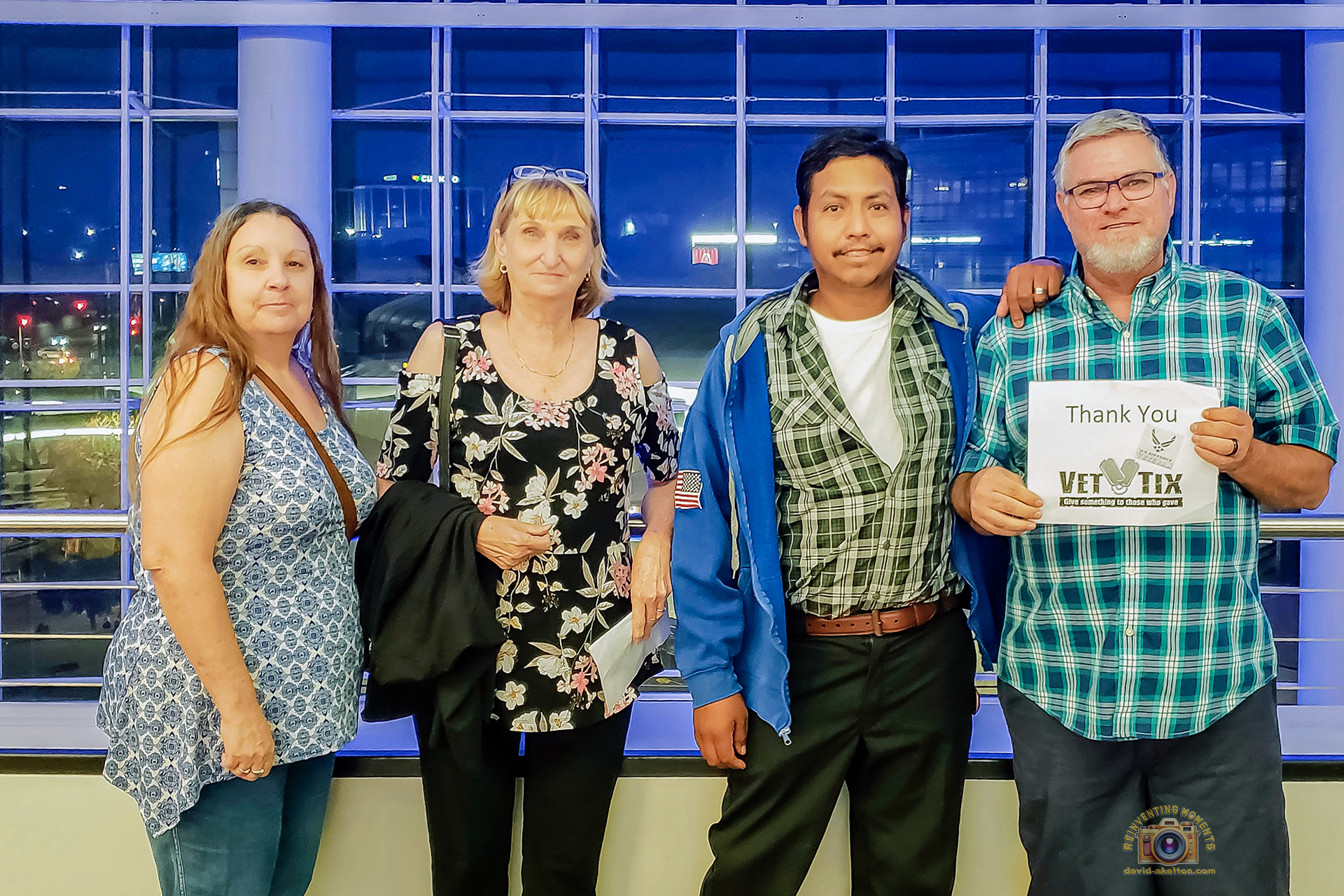 Four people, including me and my husband, Gio, standing in the glass concourse of STAPLES Center, Los Angeles, holding a "Thank You VET TIX" sign, before the Keith Urban Graffiti U Tour concert