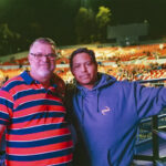David, wearing a striped polo, and Gio, in a blue hoodie, stand together in the amphitheater seats at the Greek Theatre in Los Angeles before an Evanescence concert.