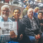 David, Gio, Robert, and Juan sitting in the amphitheater seats at Viejas Arena for the Miranda Lambert concert, while David holds a 'Thank You Vet Tix' sign.