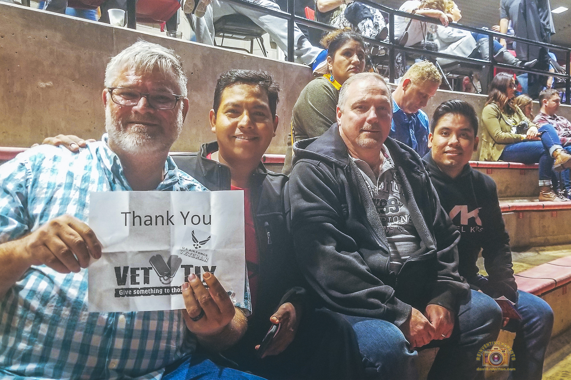 David, Gio, Robert, and Juan sitting in the amphitheater seats at Viejas Arena for the Miranda Lambert concert, while David holds a 'Thank You Vet Tix' sign.