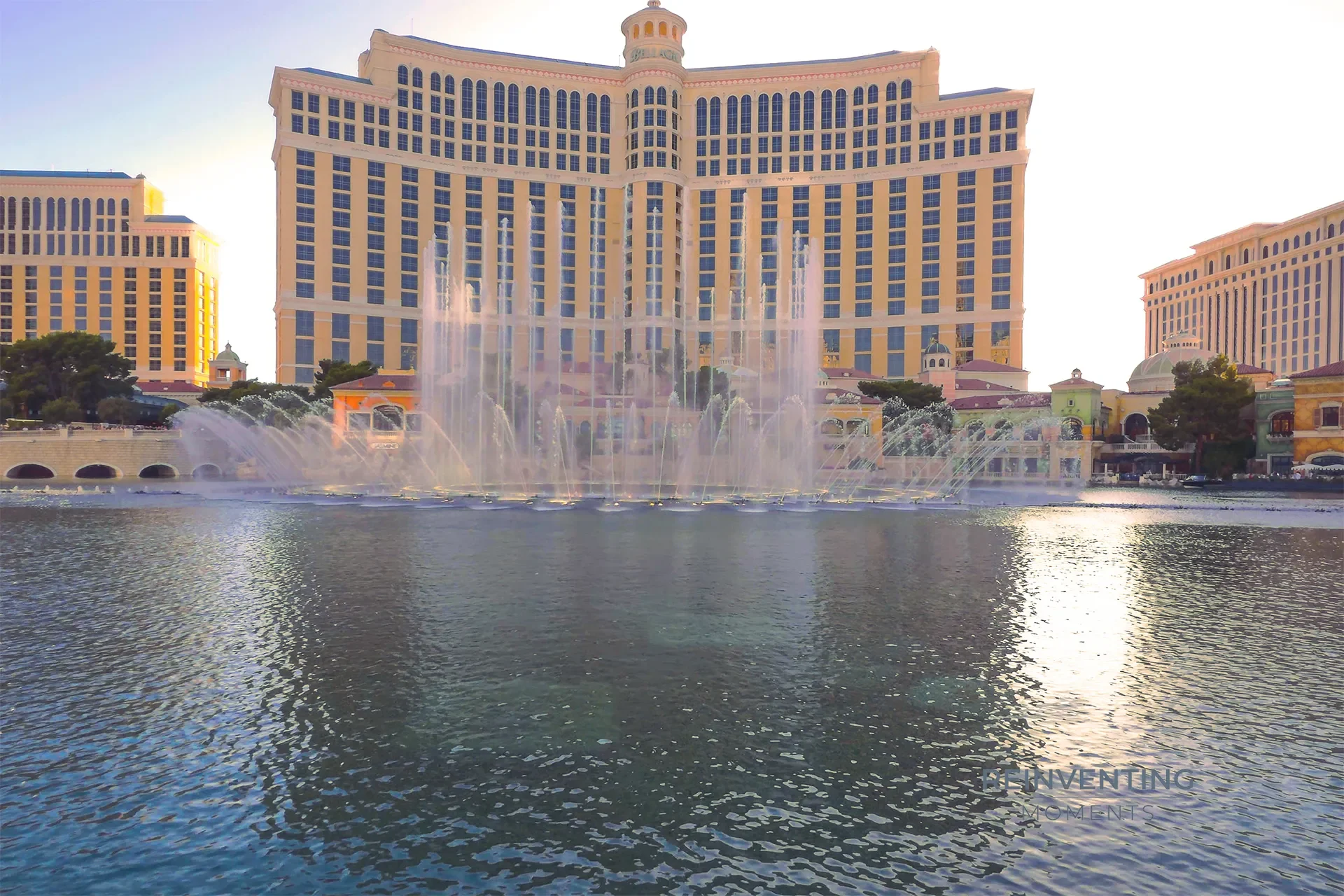 Fountains of Bellagio shooting glowing water plumes across Lake Bellagio with the resort in shadow at sunset.