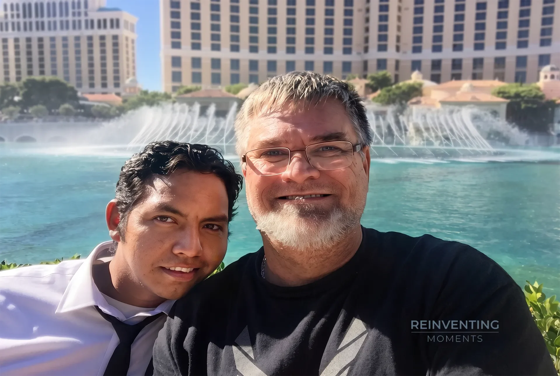 Two smiling men taking a sunny selfie in front of the Bellagio Fountains water show in Las Vegas.