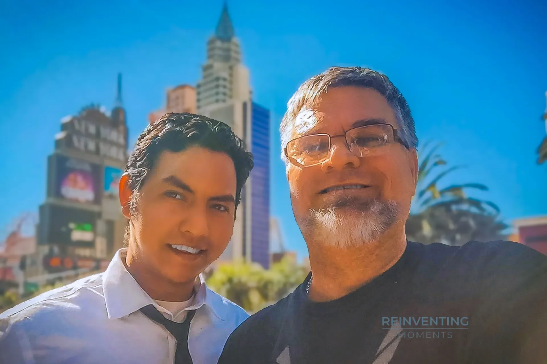 Gio and David smiling for a selfie on the Las Vegas Strip with the New York-New York casino skyline in the background.