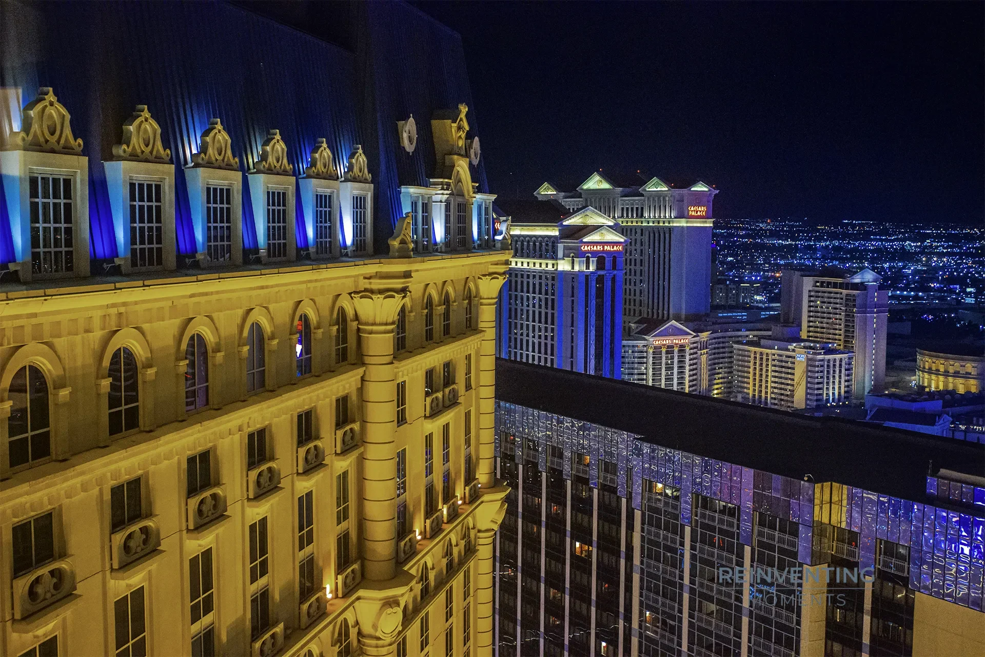 High-angle night view of the illuminated Las Vegas Strip, showing the detailed facade of Paris Las Vegas and Caesars Palace in the distance.
